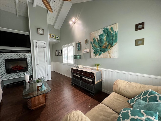 living area with vaulted ceiling with beams, a tiled fireplace, wood ceiling, wainscoting, and wood finished floors