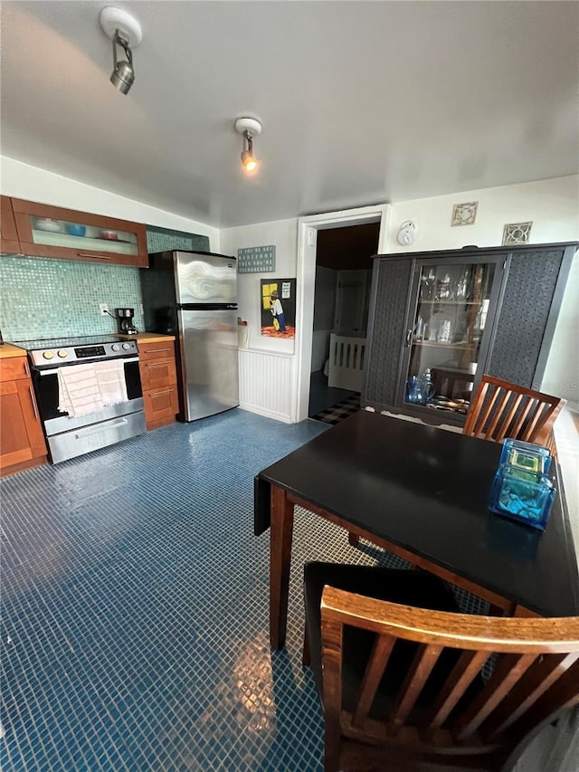 kitchen featuring wainscoting, stainless steel appliances, decorative backsplash, and exhaust hood