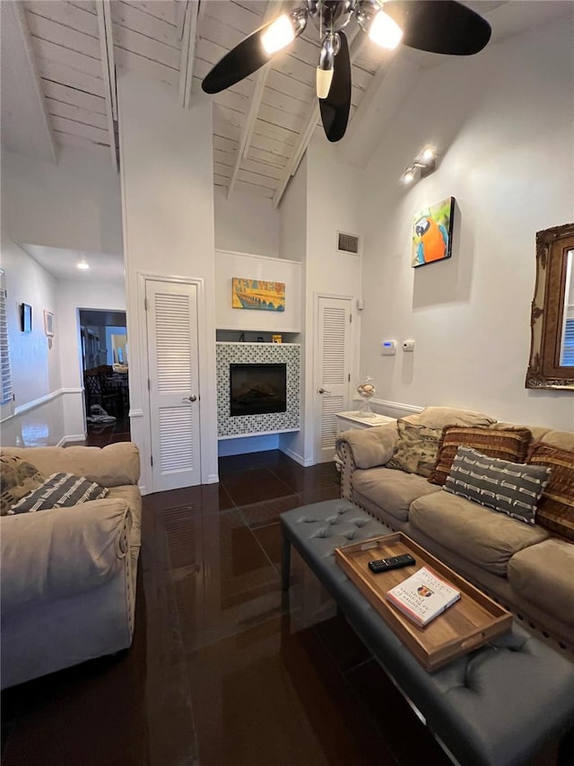 living area with a tiled fireplace, a ceiling fan, wood ceiling, high vaulted ceiling, and beam ceiling