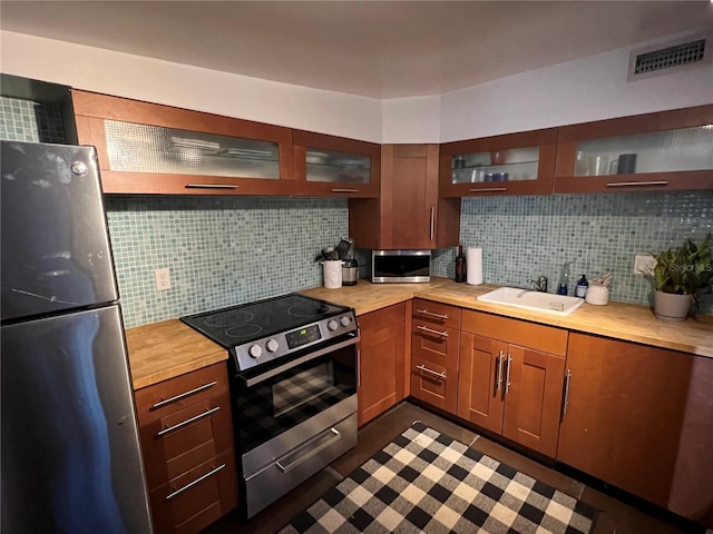 kitchen with butcher block countertops, a sink, visible vents, appliances with stainless steel finishes, and backsplash