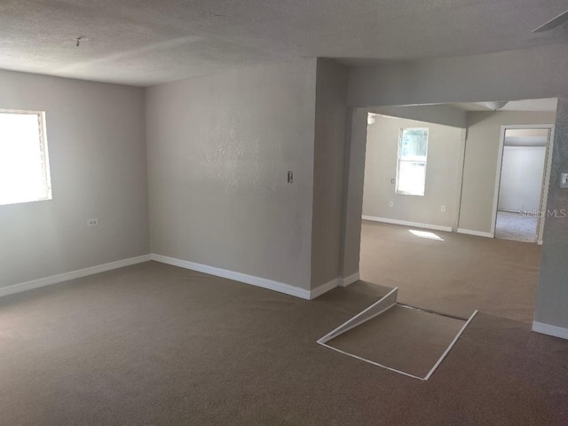 empty room with a textured ceiling, carpet flooring, and baseboards