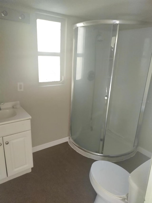 bathroom with toilet, a stall shower, baseboards, and vanity