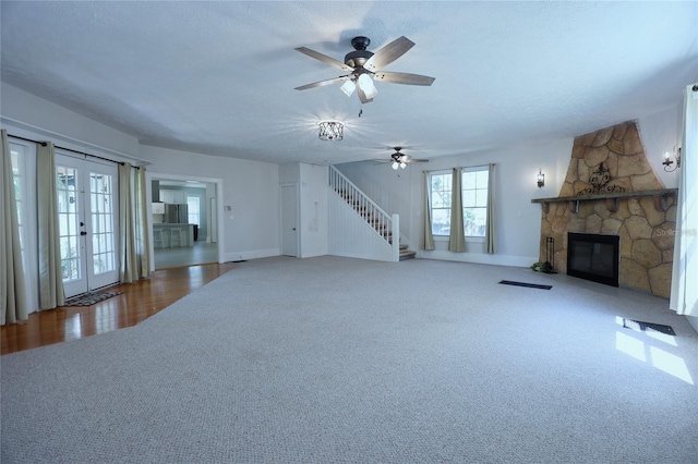 unfurnished living room featuring a textured ceiling, stairway, french doors, carpet, and a stone fireplace