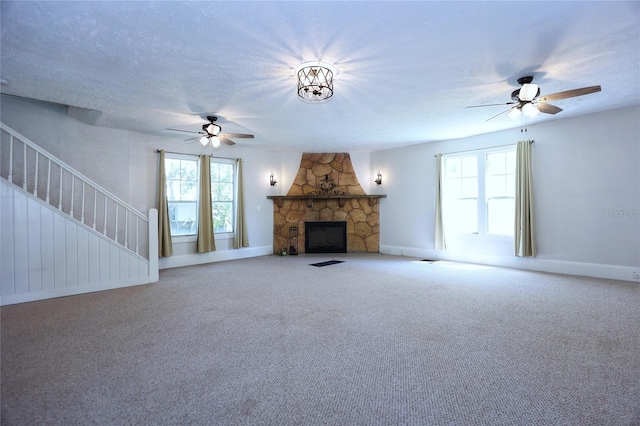 unfurnished living room featuring a stone fireplace, stairway, carpet floors, and a textured ceiling