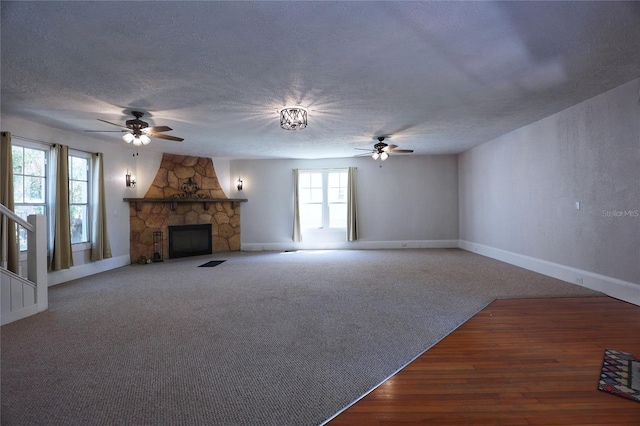 unfurnished living room with baseboards, a stone fireplace, carpet flooring, a textured ceiling, and a ceiling fan