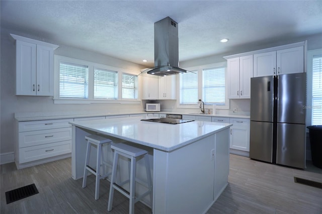 kitchen featuring visible vents, a kitchen island, island range hood, and freestanding refrigerator