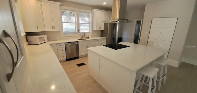 kitchen featuring visible vents, a center island, range hood, stainless steel appliances, and a sink