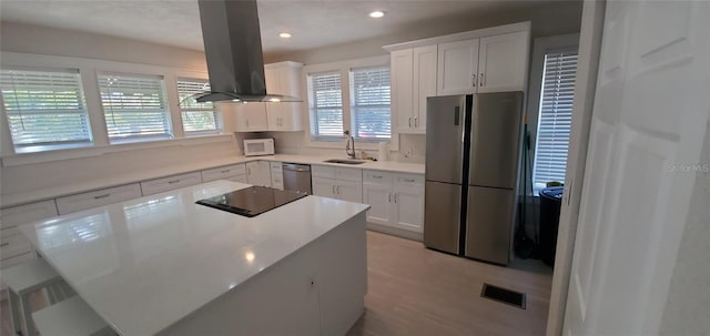 kitchen featuring visible vents, a sink, appliances with stainless steel finishes, white cabinets, and island range hood