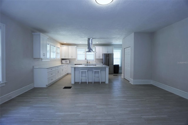 kitchen with white microwave, visible vents, baseboards, freestanding refrigerator, and wall chimney exhaust hood