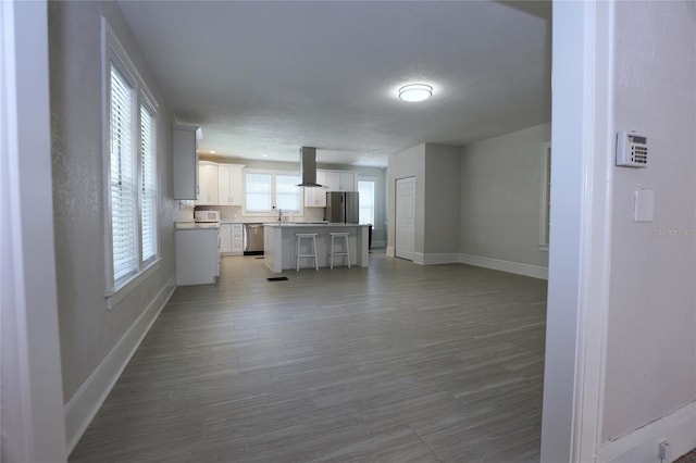 kitchen with a sink, white cabinetry, stainless steel appliances, island range hood, and baseboards