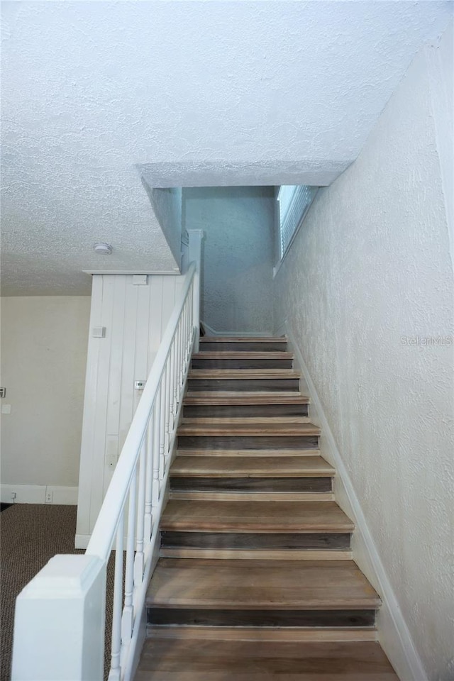 staircase featuring a textured wall, baseboards, and a textured ceiling