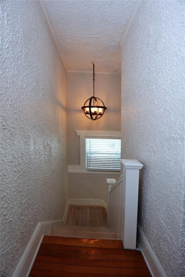 stairs featuring a textured ceiling, wood finished floors, and a textured wall