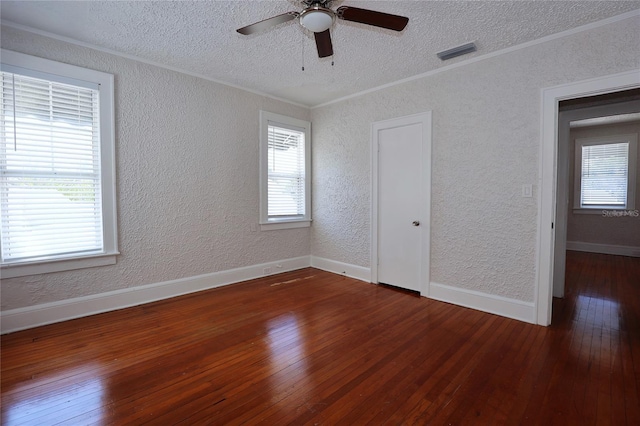 spare room with visible vents, crown molding, hardwood / wood-style floors, a textured wall, and plenty of natural light