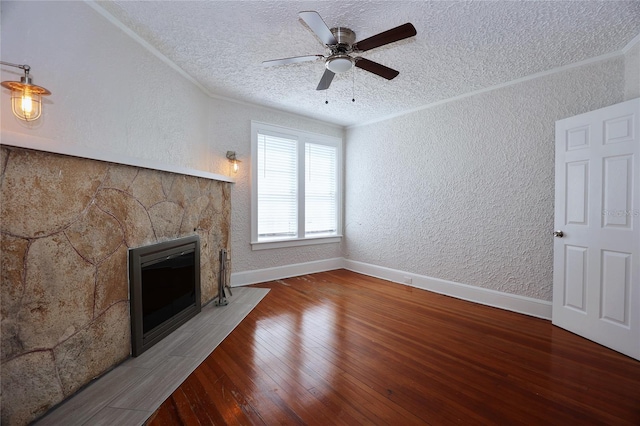 unfurnished living room featuring ornamental molding, a textured ceiling, wood finished floors, a stone fireplace, and a textured wall