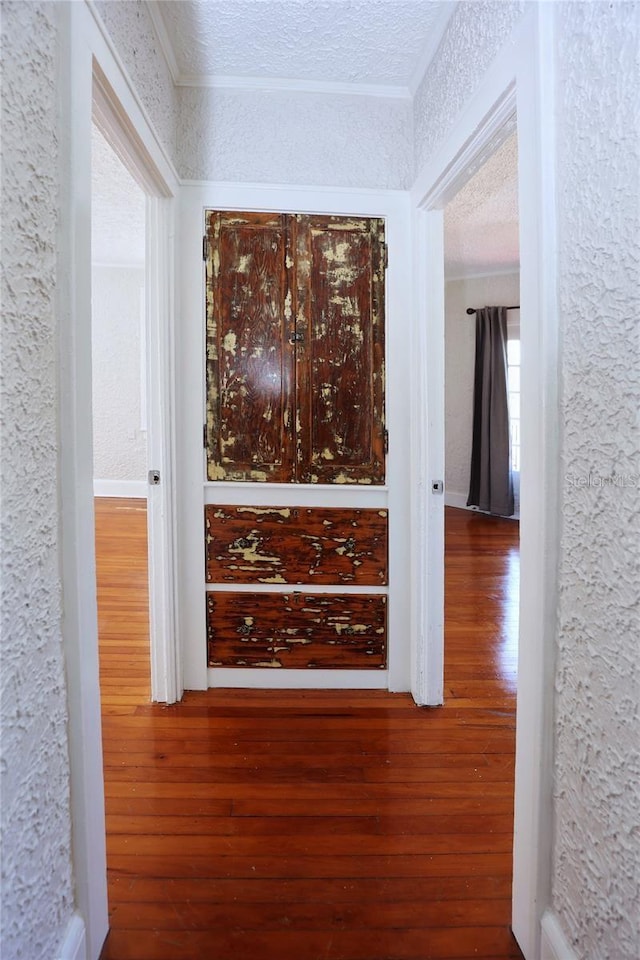 hall featuring a textured ceiling, wood finished floors, crown molding, and a textured wall