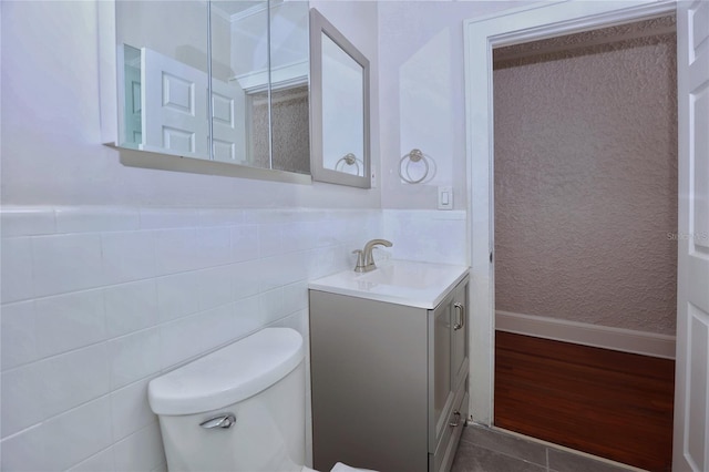 bathroom with a wainscoted wall, toilet, vanity, and tile walls