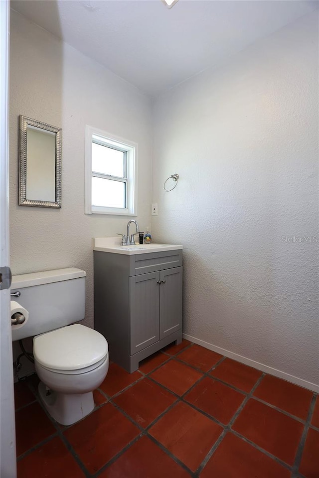 half bath featuring vanity, tile patterned floors, toilet, and baseboards