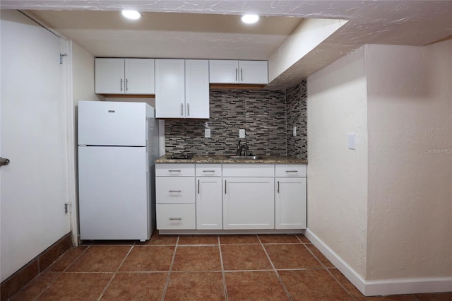 kitchen with tasteful backsplash, white cabinetry, freestanding refrigerator, and baseboards