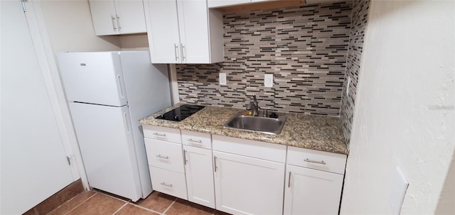 kitchen featuring black electric stovetop, decorative backsplash, freestanding refrigerator, white cabinetry, and a sink