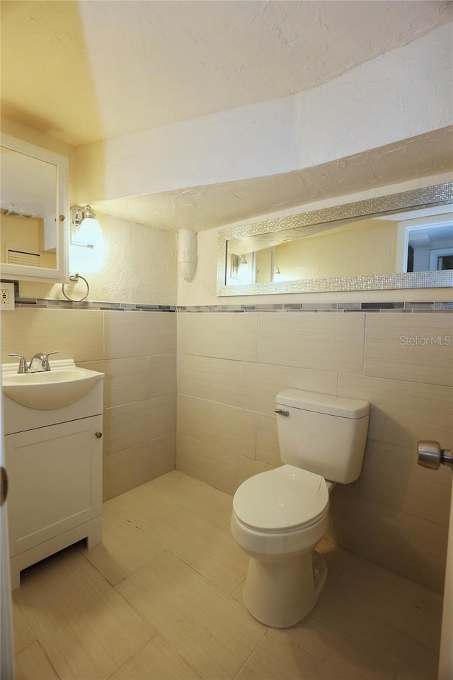 bathroom featuring toilet, tile walls, and vanity