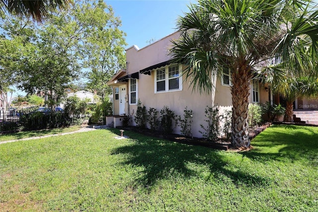 view of home's exterior with a lawn, fence, and stucco siding