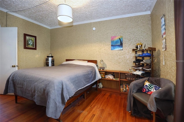 bedroom featuring wood finished floors, a textured ceiling, ornamental molding, and a textured wall