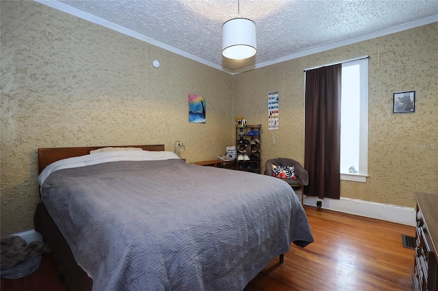 bedroom with visible vents, a textured ceiling, wood finished floors, and crown molding