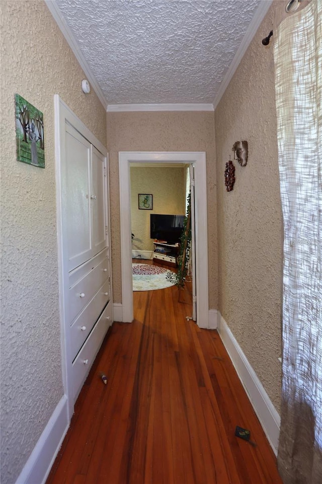 hall featuring a textured ceiling, a textured wall, wood-type flooring, and ornamental molding