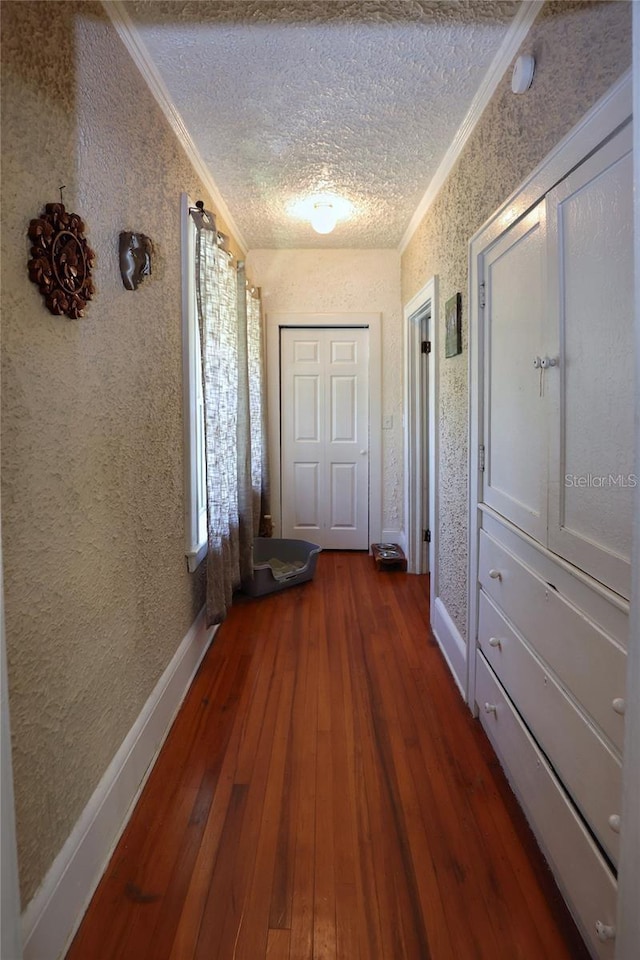 hallway with dark wood-type flooring, a textured ceiling, ornamental molding, and wallpapered walls