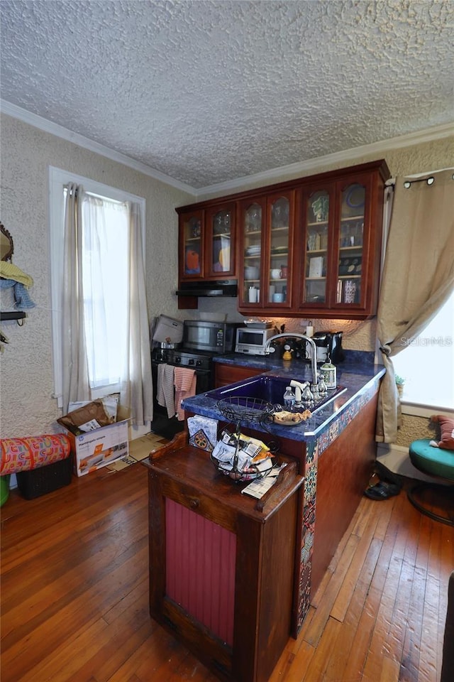 interior space with ornamental molding, stainless steel microwave, dark countertops, hardwood / wood-style floors, and glass insert cabinets