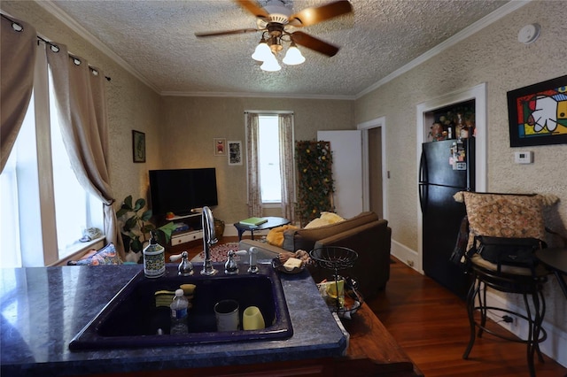 living area with wood finished floors, ceiling fan, a textured ceiling, crown molding, and a textured wall