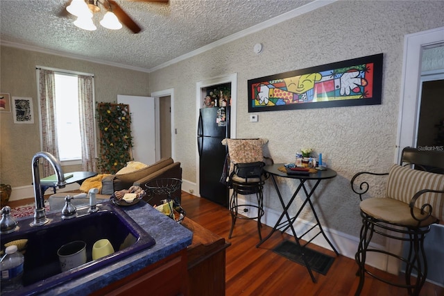 kitchen featuring dark wood-type flooring, a sink, a textured ceiling, freestanding refrigerator, and crown molding