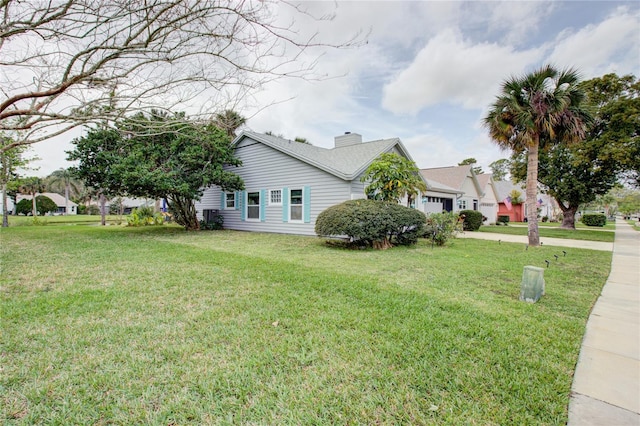 view of side of property featuring a chimney, a lawn, driveway, and an attached garage