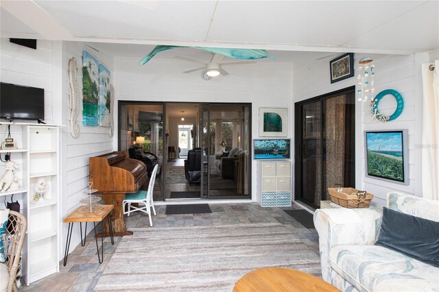 interior space with a ceiling fan, stone finish floor, wood walls, and a sunroom