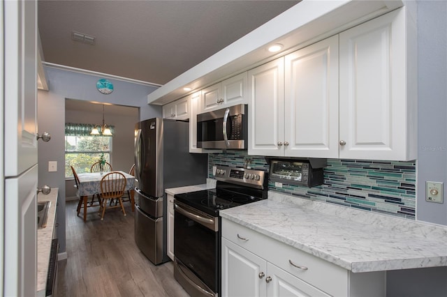 kitchen with stainless steel appliances, visible vents, white cabinetry, decorative backsplash, and light wood finished floors