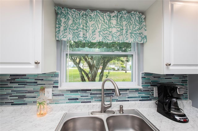 kitchen with tasteful backsplash, white cabinetry, a sink, and light stone countertops