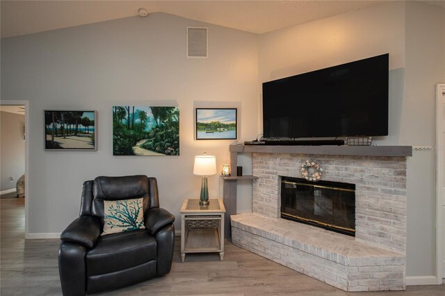 living room with a brick fireplace, visible vents, vaulted ceiling, and wood finished floors