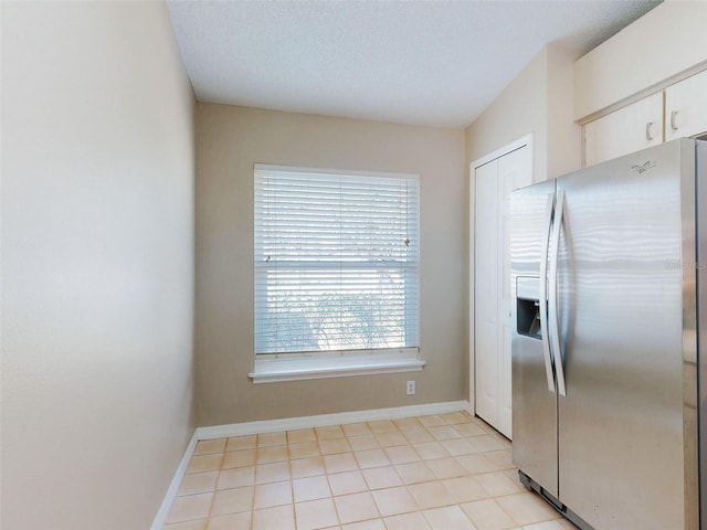 kitchen with stainless steel fridge, baseboards, a textured ceiling, and light tile patterned flooring