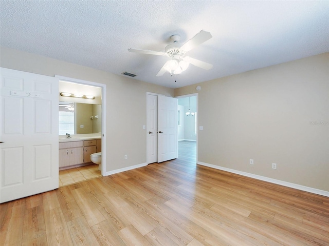 unfurnished bedroom featuring a textured ceiling, connected bathroom, visible vents, baseboards, and light wood-type flooring