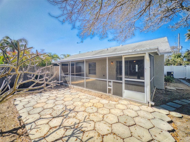 rear view of property featuring a patio area, a sunroom, a fenced backyard, and stucco siding