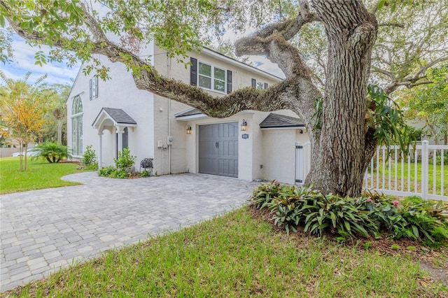 view of front of home with a garage, fence, decorative driveway, a front lawn, and stucco siding