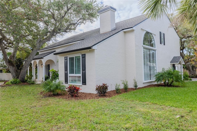 view of side of property with roof with shingles, a chimney, a lawn, and stucco siding