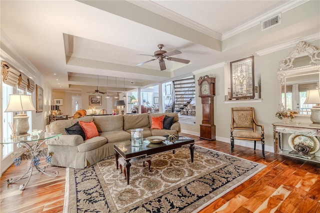 living room with visible vents, a raised ceiling, a ceiling fan, stairs, and crown molding