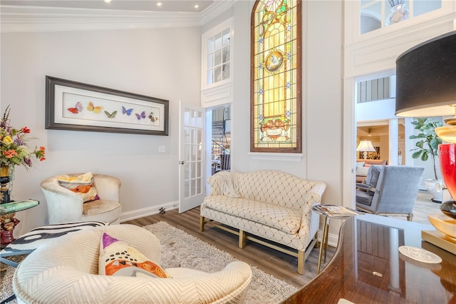 sitting room featuring baseboards, a high ceiling, ornamental molding, and wood finished floors