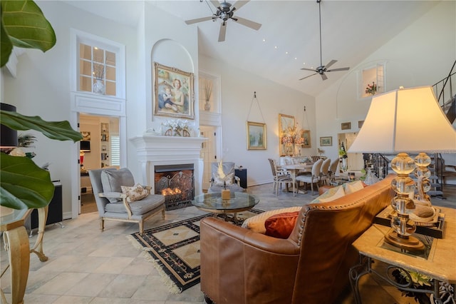 living room with high vaulted ceiling, a warm lit fireplace, and a ceiling fan