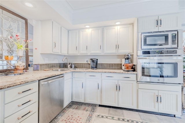 kitchen with light tile patterned floors, light stone counters, stainless steel appliances, white cabinets, and ornamental molding