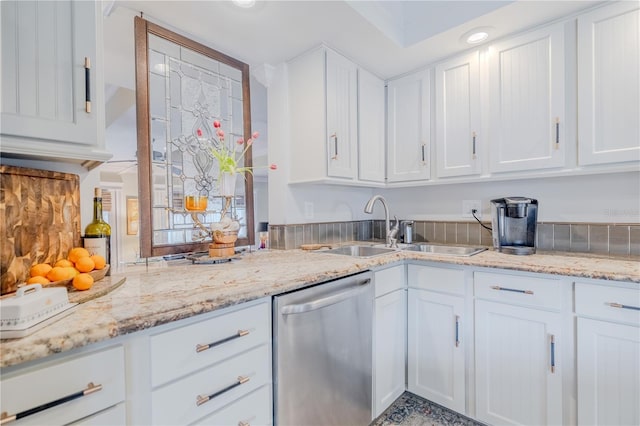 kitchen with a sink, light stone counters, white cabinets, and dishwasher