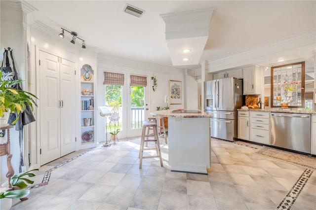 kitchen with a breakfast bar area, stainless steel appliances, a kitchen island, visible vents, and ornamental molding