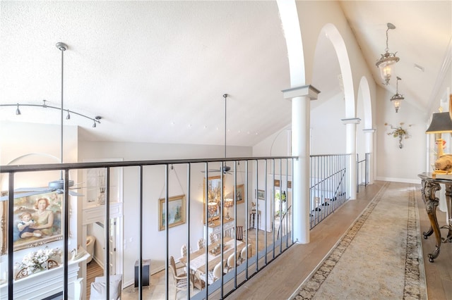 hall featuring lofted ceiling, a textured ceiling, arched walkways, baseboards, and ornate columns