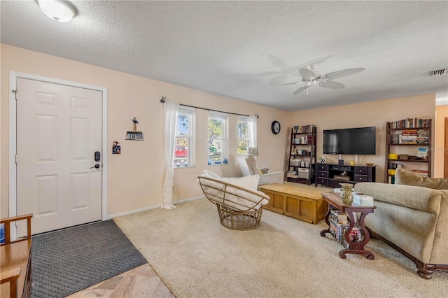 carpeted living area featuring baseboards, ceiling fan, visible vents, and a textured ceiling